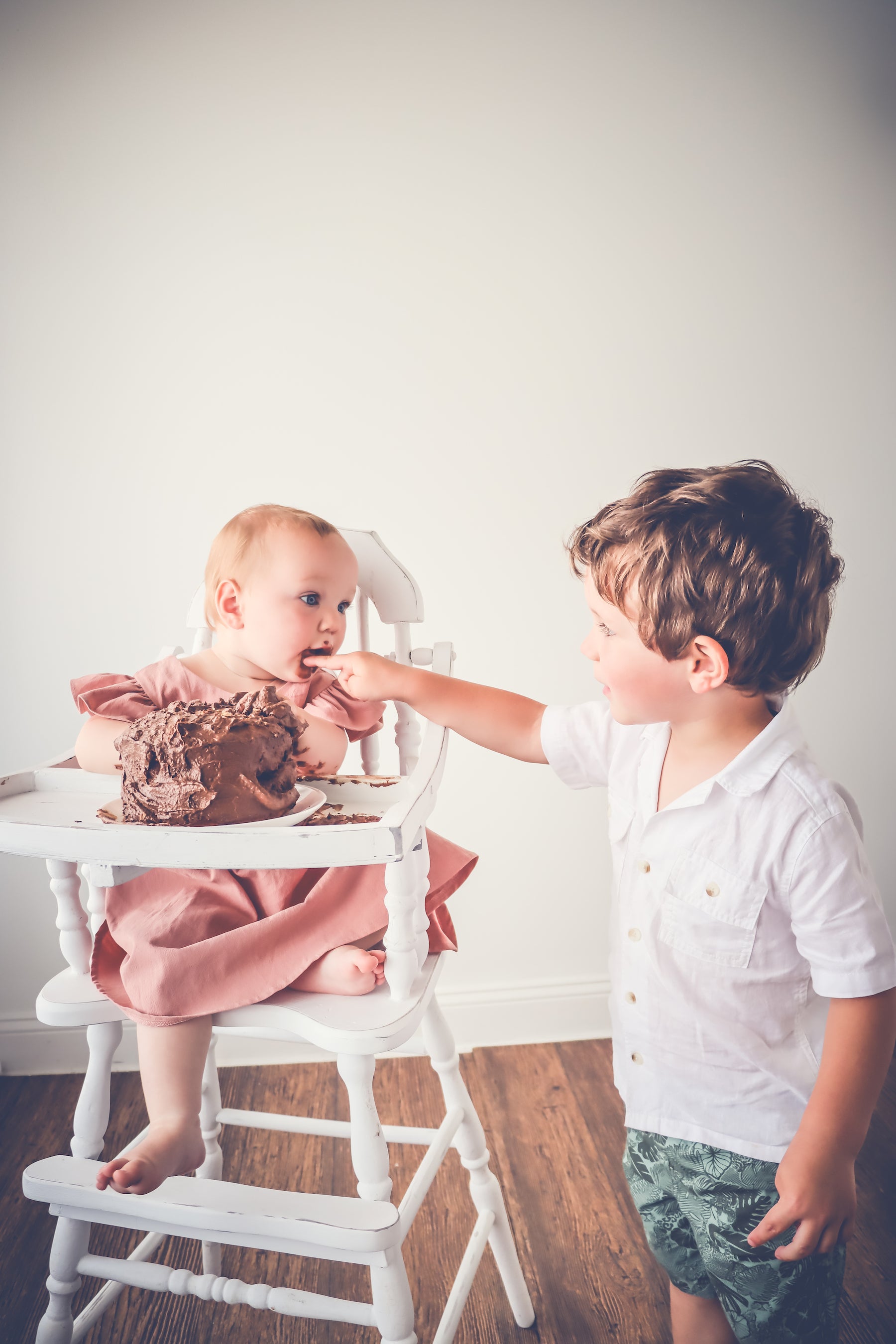 A baby smashing a chocolate cake with a sibling 